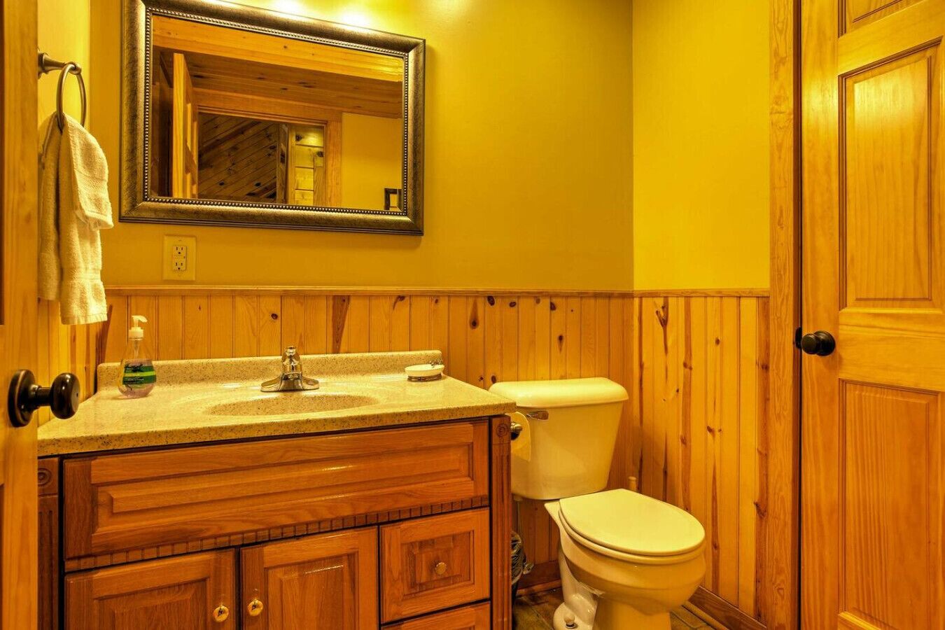 A bathroom with wooden paneling, a sink with a mirror above it, and a toilet.