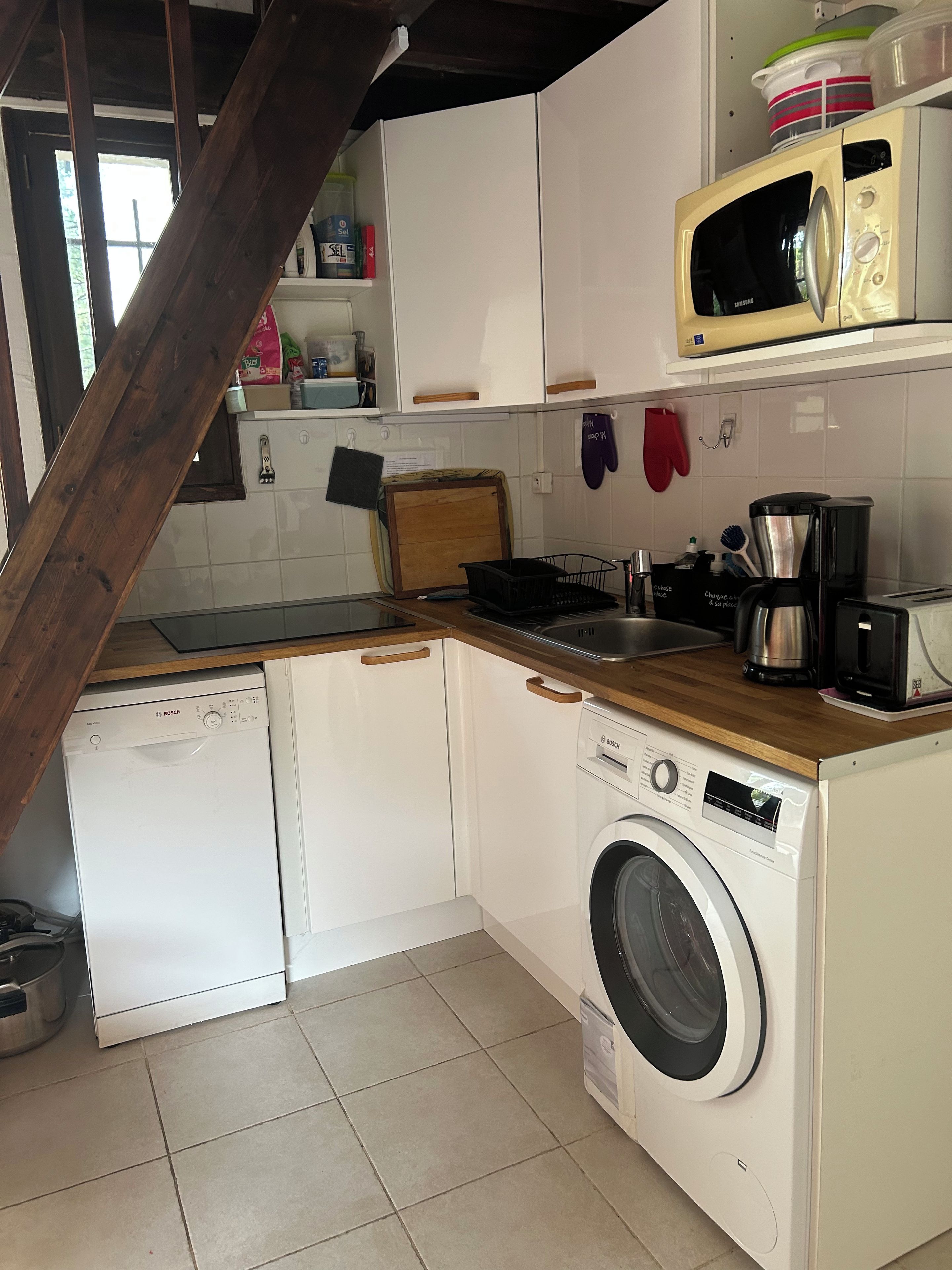 A compact kitchen with a dishwasher, washing machine, microwave, and a coffee maker.