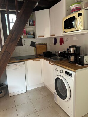 A compact kitchen with a dishwasher, washing machine, microwave, and a coffee maker.