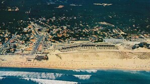 Una vista aerea di una cittadina costiera con una spiaggia, una fortificazione e una zona urbana densa.