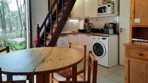 Una cucina compatta con lavatrice, forno a microonde e mobili in legno. In primo piano, un tavolo e sedie di legno.