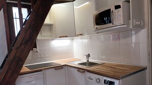 Una cucina compatta con mobili bianchi, un piano di lavoro in legno, un lavello, un forno a microonde e una lavatrice Bosch.