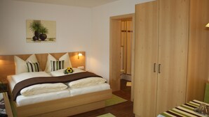 Een slaapkamer met een houten bed, nachtkastje, schilderij aan de muur en een houten kledingkast.