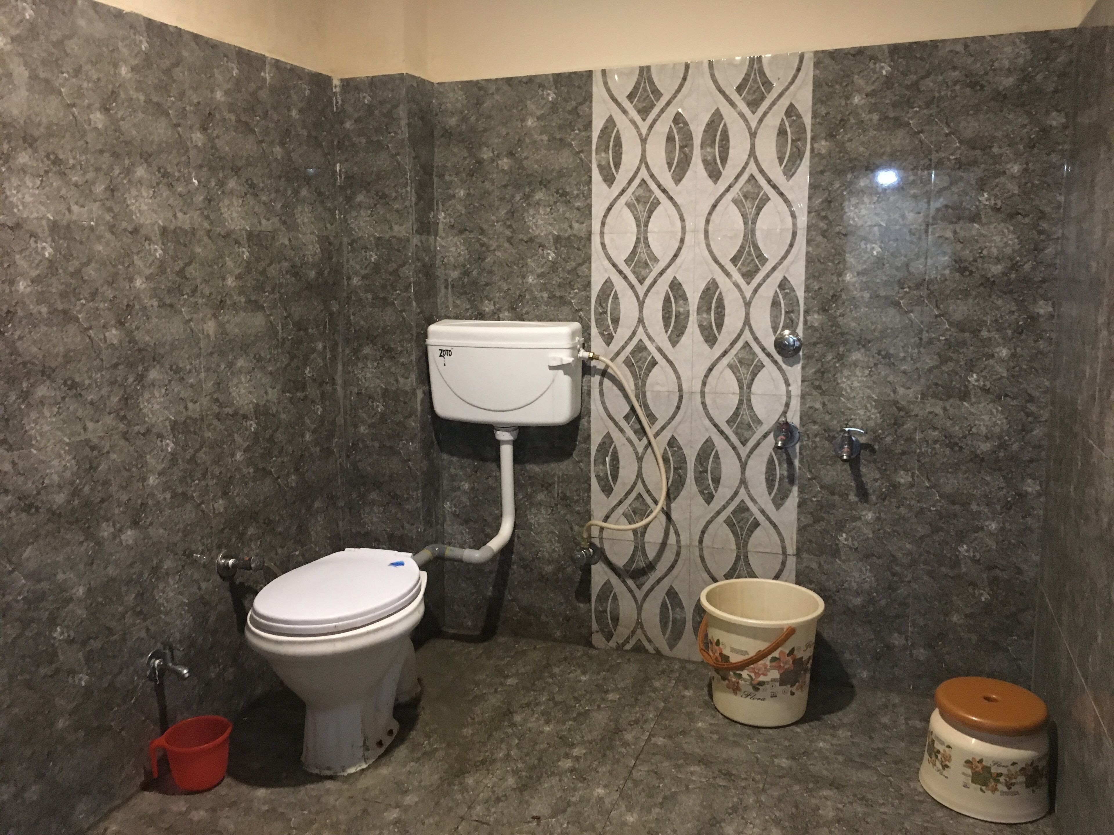 A bathroom with a toilet, a bidet, a red bucket, and a decorative bucket.