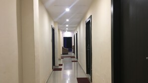 A long, narrow hallway with doors on both sides, leading to rooms. The floor is tiled, and there are red mats at the door entrances. - Hotel Duke Inn (Jhansi)