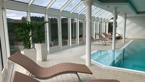 A sunlit indoor swimming pool area with lounge chairs and potted plants.