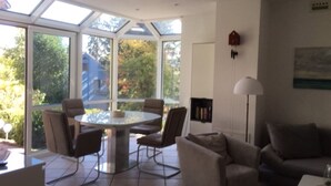 A modern living room with a glass dining table surrounded by chairs, a sofa, and a lamp.