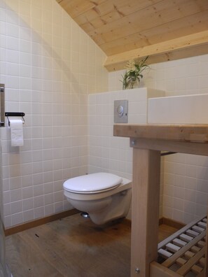 Un baño pequeño y limpio con azulejos blancos, piso de madera y un inodoro blanco.