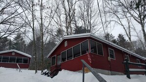 Eine rote Holzhütte mit weißem Zaun, umgeben von schneebedecktem Boden und Bäumen.