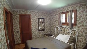 Ein Schlafzimmer mit Bett, Nachttisch, Spiegel und einem Fenster mit Vorhängen.