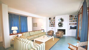 A living room with striped sofas, a coffee table, a bookshelf, and a fireplace.