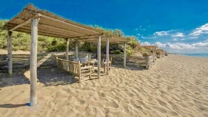 Ein Strand mit Holzkonstruktionen als Sonnenschutz, feinem Sand und blauem Himmel.