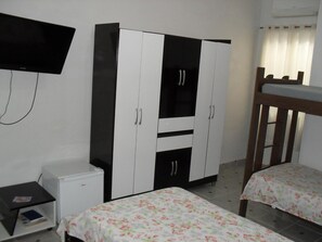 A bedroom with a bunk bed, a small white refrigerator, a TV mounted on the wall, and a wardrobe with two doors.