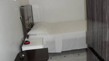 Una habitación pequeña con una cama individual, escritorio, silla, espejo y ventana.