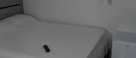 A single bed with a remote control on it, a small bedside table, and a wall socket.