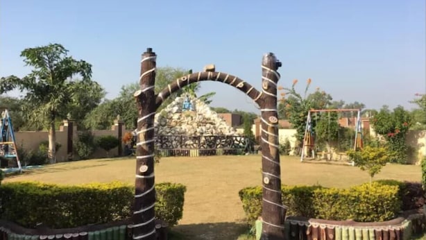 An outdoor area with a decorative archway, a playground, and a pile of construction materials in the background.