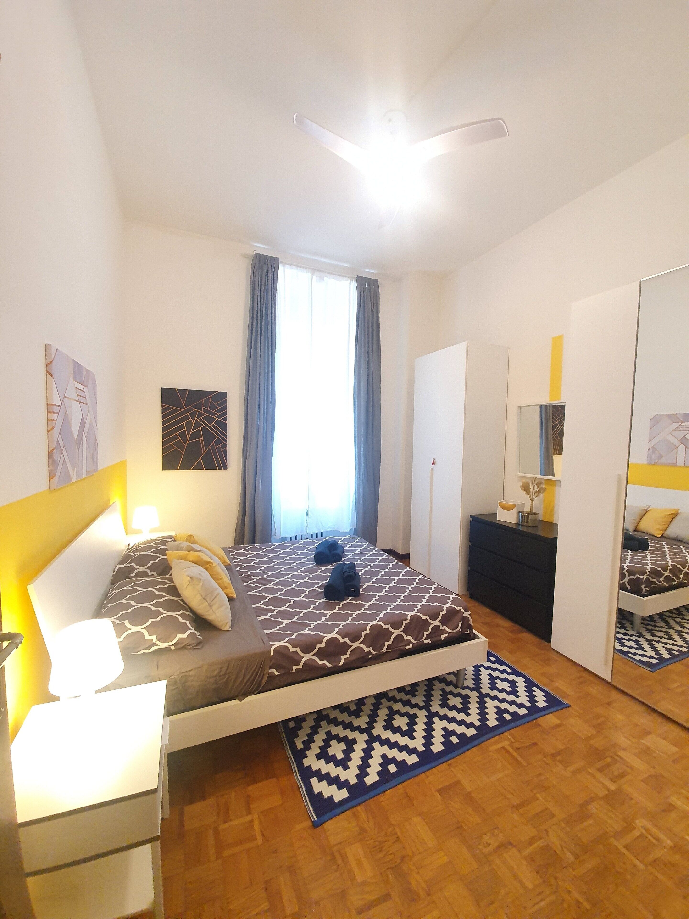 A modern bedroom with a bed, bedside tables, a mirror, and a wardrobe.