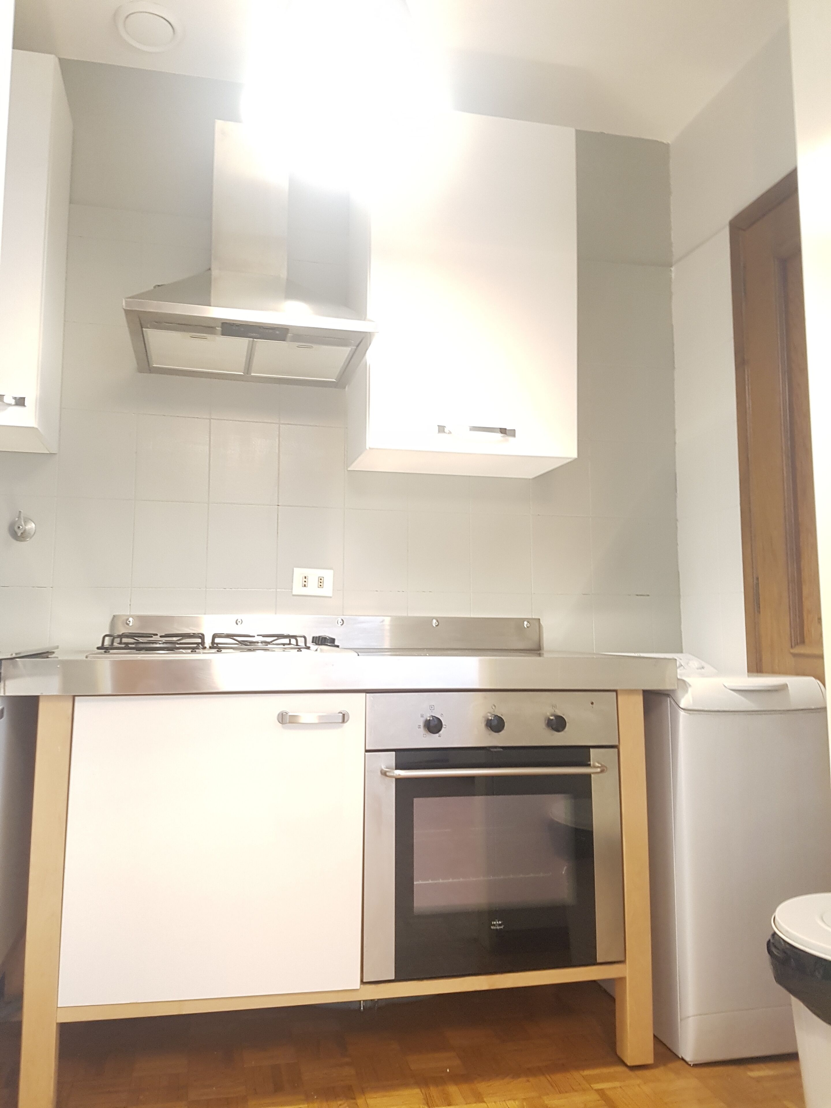 A kitchen with white cabinets, a stainless steel stove, an oven, and a trash bin.