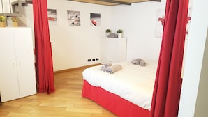 A bedroom with a bed, red curtains, a wardrobe, a small desk, and wall art. - Casa Maltese (Turin)