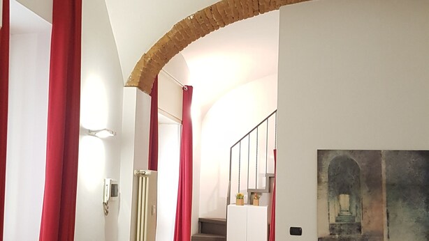 A spacious living area with a wooden floor, red curtains, a staircase, a flat-screen TV, and a painting on the wall. - Casa Maltese (Turin)