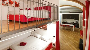 A dormitory-style room with bunk beds, a small table, and a kitchenette. - Casa Maltese (Turin)