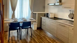 Una cucina moderna con zona pranzo, caratterizzata da pavimento in legno, mobili chiari e una finestra con tende.