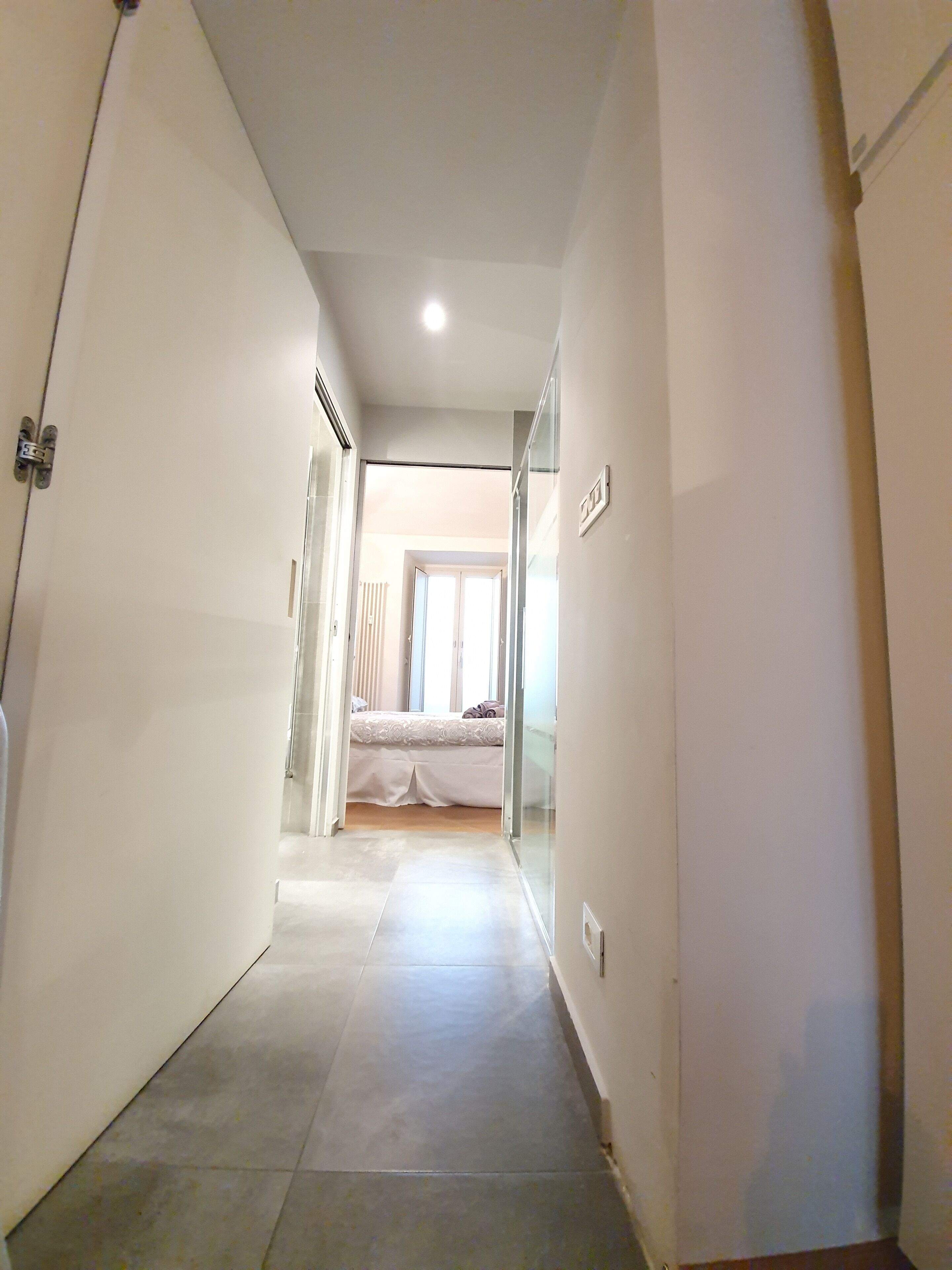 A narrow hallway with a bed in the background, leading to a room with a window.