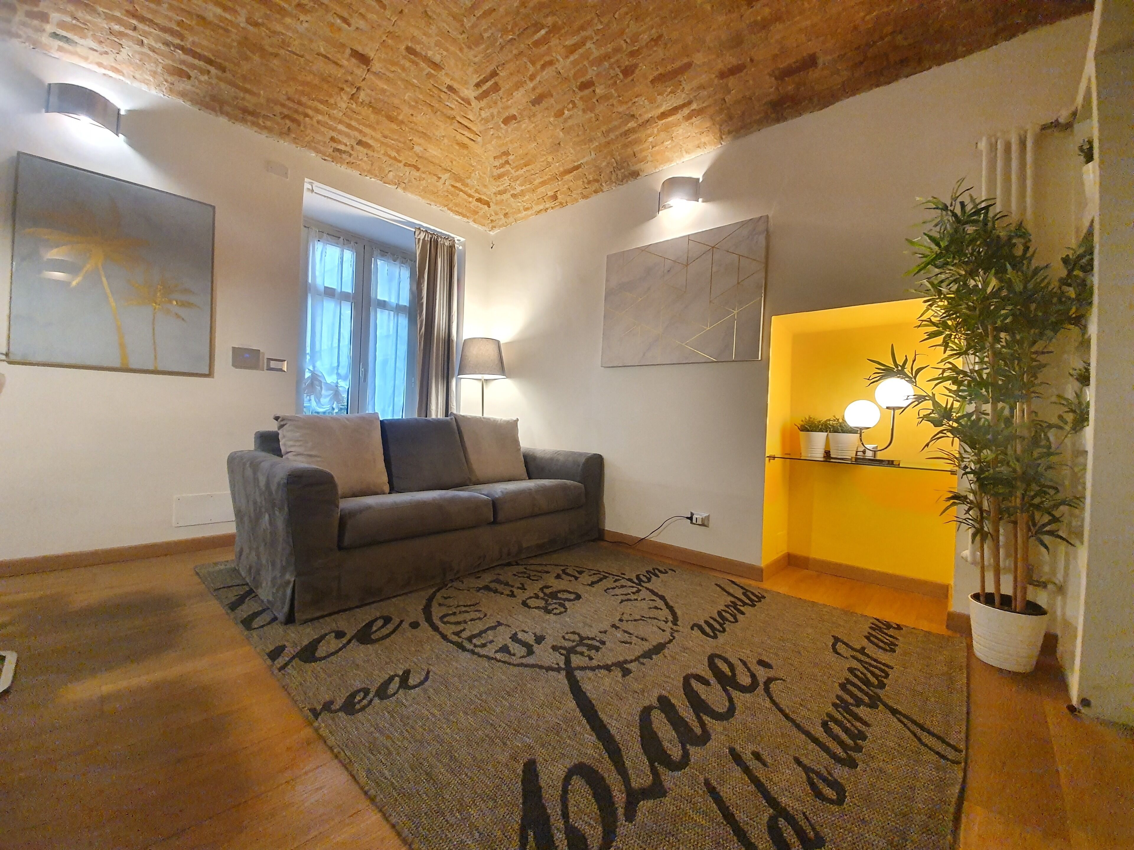 A cozy living room with a wooden ceiling, a grey sofa, a patterned rug, and a yellow accent wall.