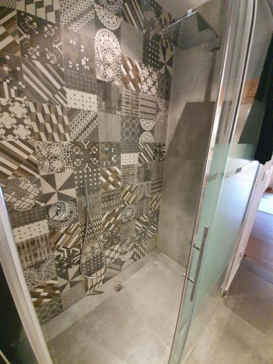 A shower area with a glass door and a tiled wall featuring various geometric patterns.