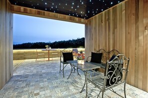 En udendørs terrasse med træterrasse, metalstole, et bord og udsigt over landskabet.