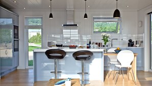 Una cocina moderna con una isla central, dos taburetes de bar, una mesa de madera e iluminación colgante.