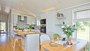 A modern kitchen with white cabinetry, a wooden island, and a dining area with a table set for two. - Perry Lodge, Strawberryfield Park - Hot Tub - Free Parking & WiFi (Cheddar)