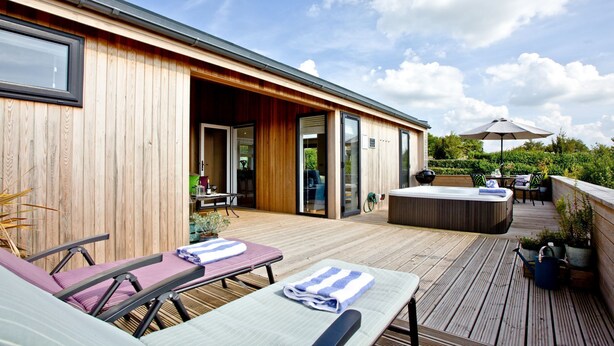 A wooden deck with lounge chairs and a hot tub, a covered patio area, and a view of the surrounding greenery. - Perry Lodge, Strawberryfield Park - Hot Tub - Free Parking & WiFi (Cheddar)
