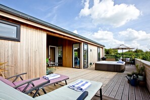 Une terrasse en bois avec des chaises longues et un jacuzzi, un patio couvert et une vue sur la verdure environnante.