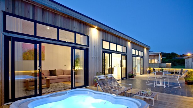 Une maison moderne dotée d’un jacuzzi, d’un espace salon extérieur et d’une grande porte-fenêtre coulissante donnant sur un espace de vie.