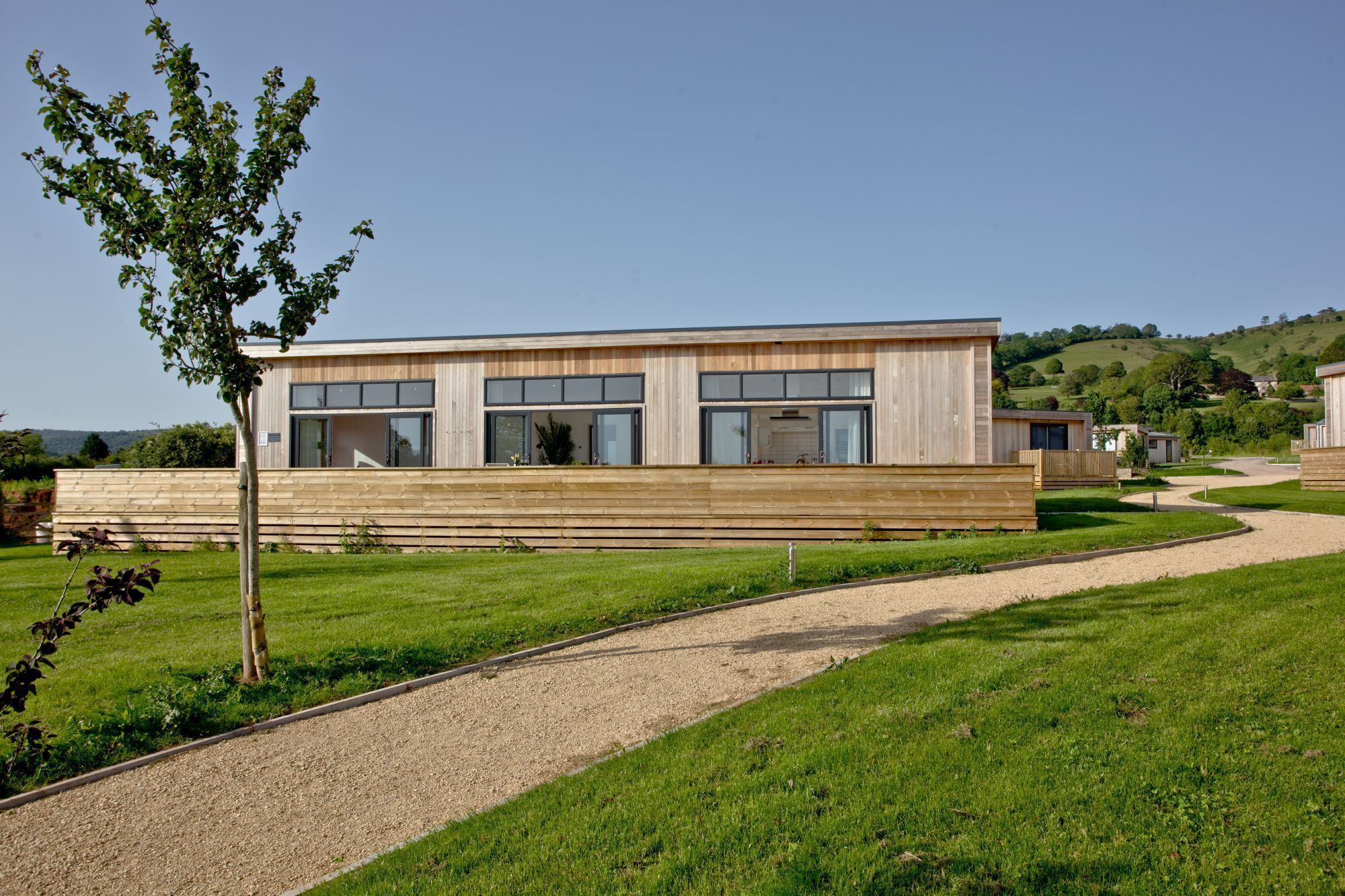 A modern building with large windows and a wooden facade, surrounded by a well-maintained lawn and a gravel path.