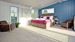 A bedroom with a bed, two chairs, a bedside table, and a window with blinds. - Batcombe Hollow, Strawberryfield Park (Cheddar)