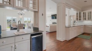 A spacious kitchen with white cabinetry, a built-in dishwasher, and a large island with a sink. - Bourbon Breeze - Beachy Home Near the Gulf with Spacious Outdoor Pool Area (Miramar Beach)