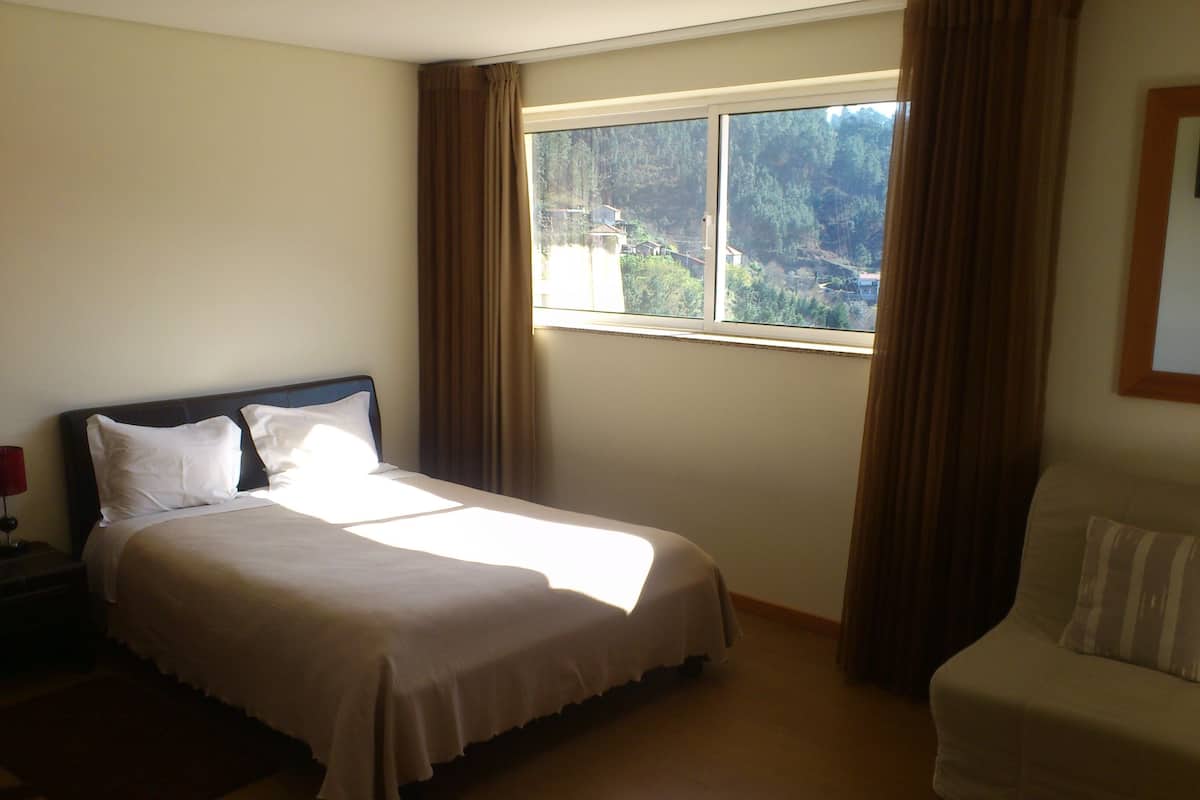 A hotel room with a bed, a chair, and a window with curtains.