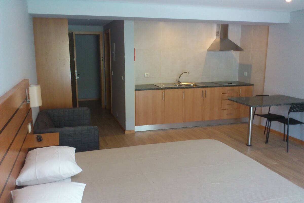 A compact hotel room with a bed, a small kitchenette, a dining table with chairs, and a separate seating area.
