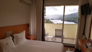 Habitació d'hotel amb llit, escriptori, cadira i vista a un llac i muntanyes.