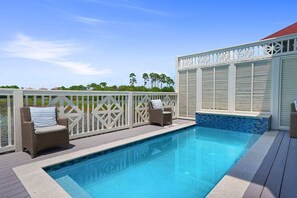 Piscina con dos sillas de mimbre y una valla blanca.