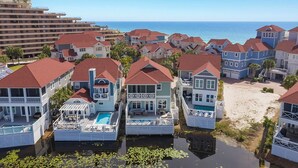 A coastal residential area with houses featuring red roofs and white exteriors, a swimming pool, and a view of the ocean. - Don't Worry Beach Happy - Lakefront Vacation Home Near the Beach with a Private Pool (Miramar Beach)