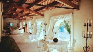 An indoor dining area with white tables and chairs, a chandelier, and a view of greenery outside. - ANTICO FEUDO SICILIANO (Syracuse)