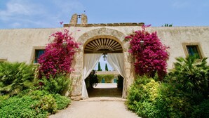 An arched entrance with a bell, surrounded by lush greenery and flowering plants. - ANTICO FEUDO SICILIANO (Syracuse)