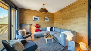 A modern living room with a grey sofa, a round coffee table, and a wooden ceiling. There are two framed pictures on the wall and a red vase with flowers. - Luxury flat for 8 people - modern, central, ski in ski out (Châtel)