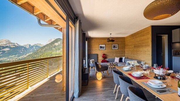 A modern dining area with a wooden deck overlooking mountains, a large table set for dining, and a cozy seating area with a sofa and chairs. - Luxury flat for 8 people - modern, central, ski in ski out (Châtel)