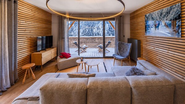 A modern living room with a large sofa, a television, and a painting on the wall. - Flat 6 pers - modern, central, ski in ski out (Châtel)