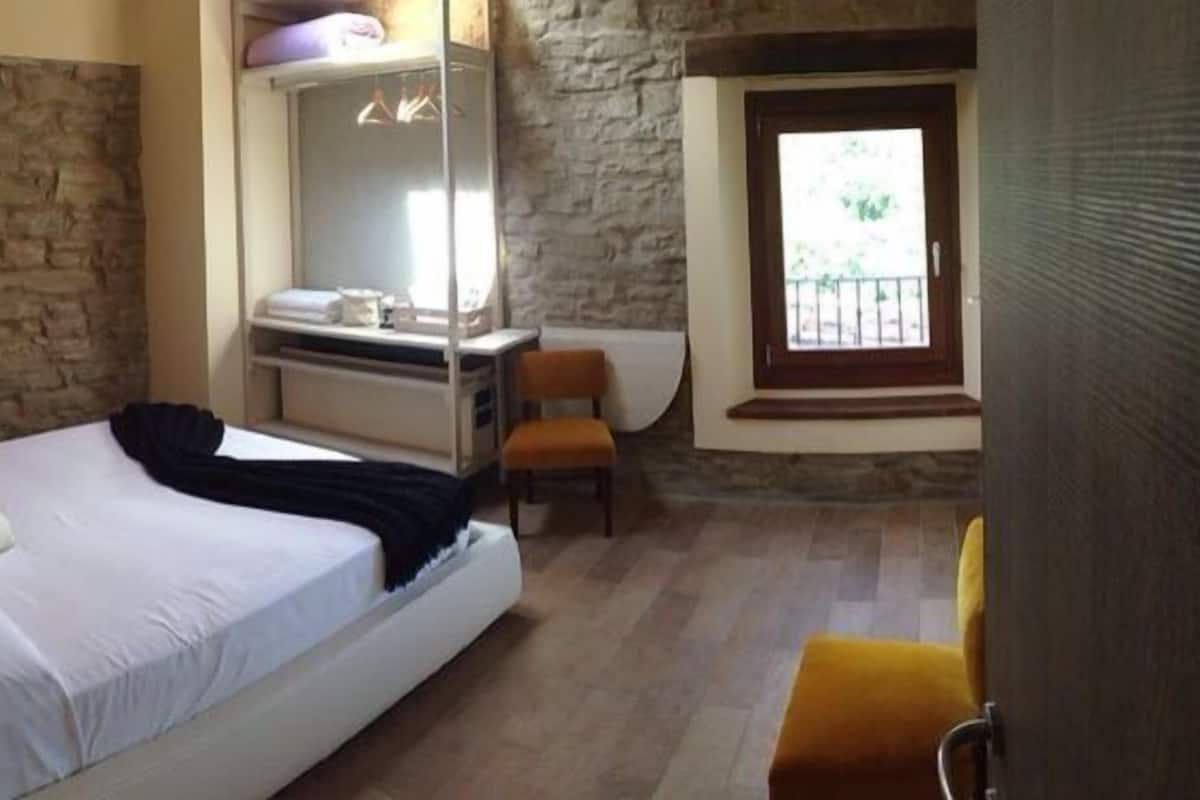 A bedroom with a stone wall, a bed, a desk, and a window.