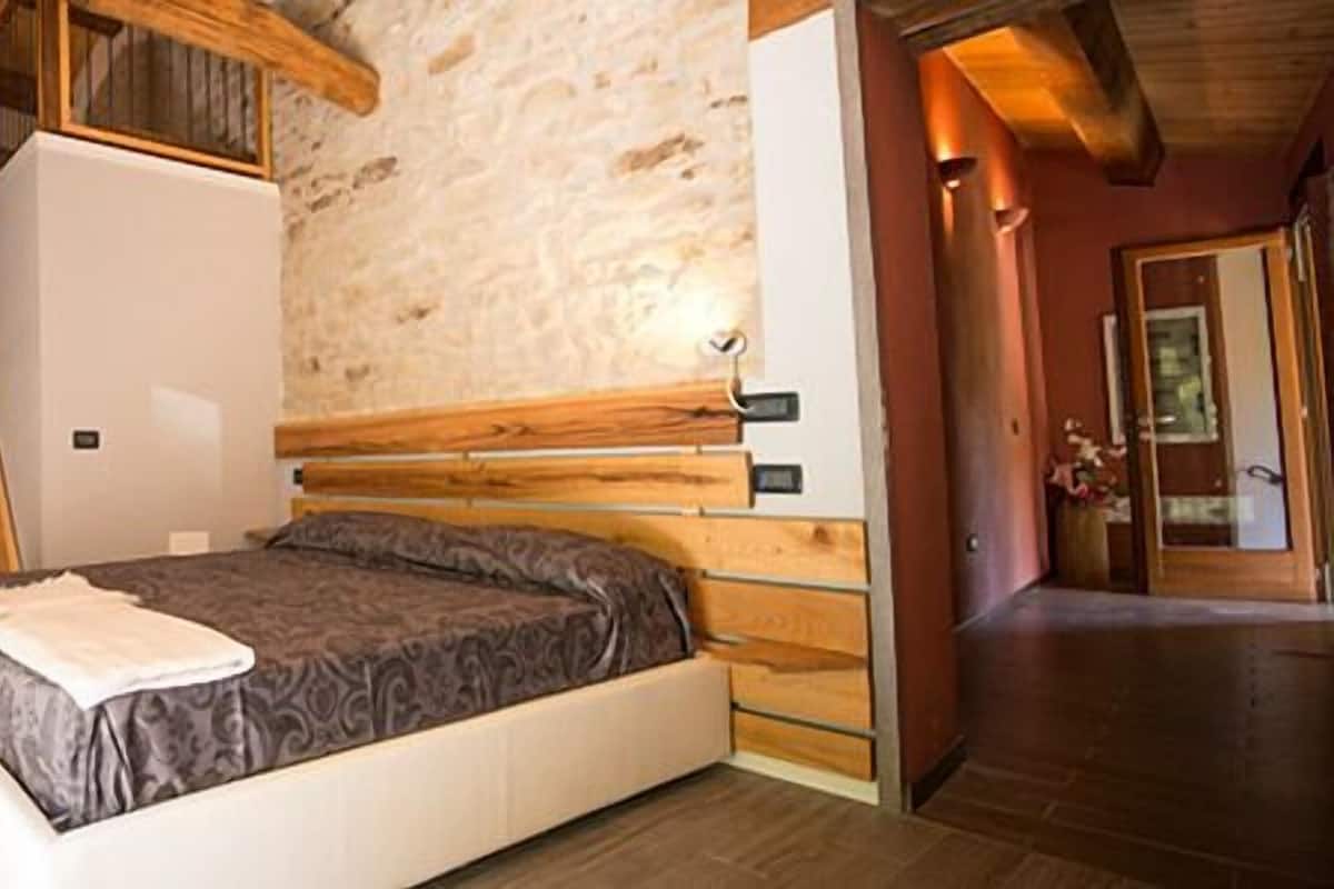 A bedroom with a bed, a wooden headboard, a staircase, and a stone wall.